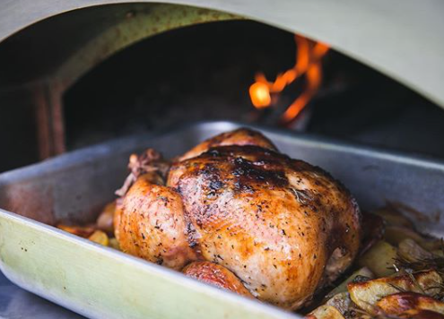 A whole roast chicken in pan and a fireplace