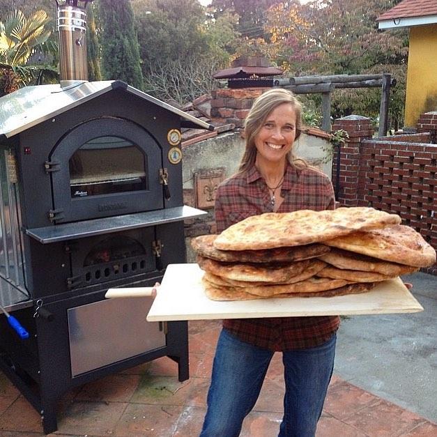 senior Woman holding pizza naan standing front of outdoor Pizza Ovens