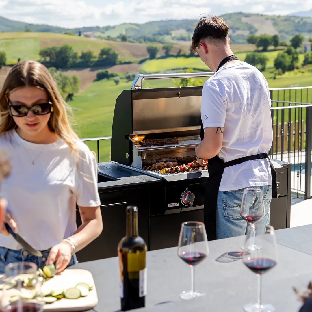 Young couple grilling kebabs and prepping vegetables with wine glasses on countertop of Elysia Outdoor Kitchen