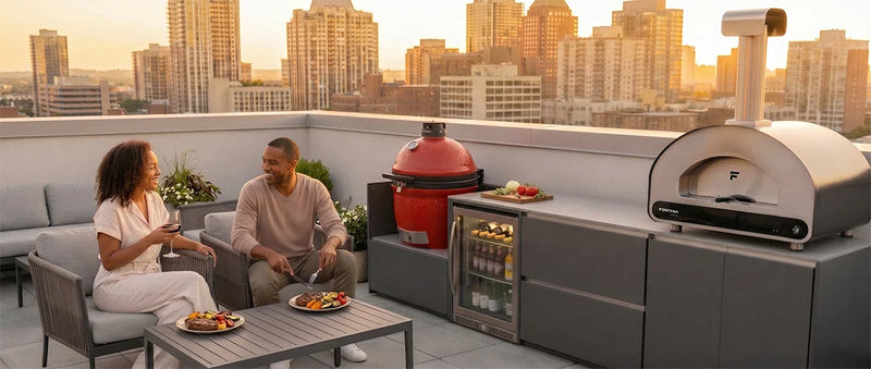 Ember outdoor modular kitchen with two people enjoying a meal on a rooftop with a cityscape view, featuring a pizza oven and refrigerator.