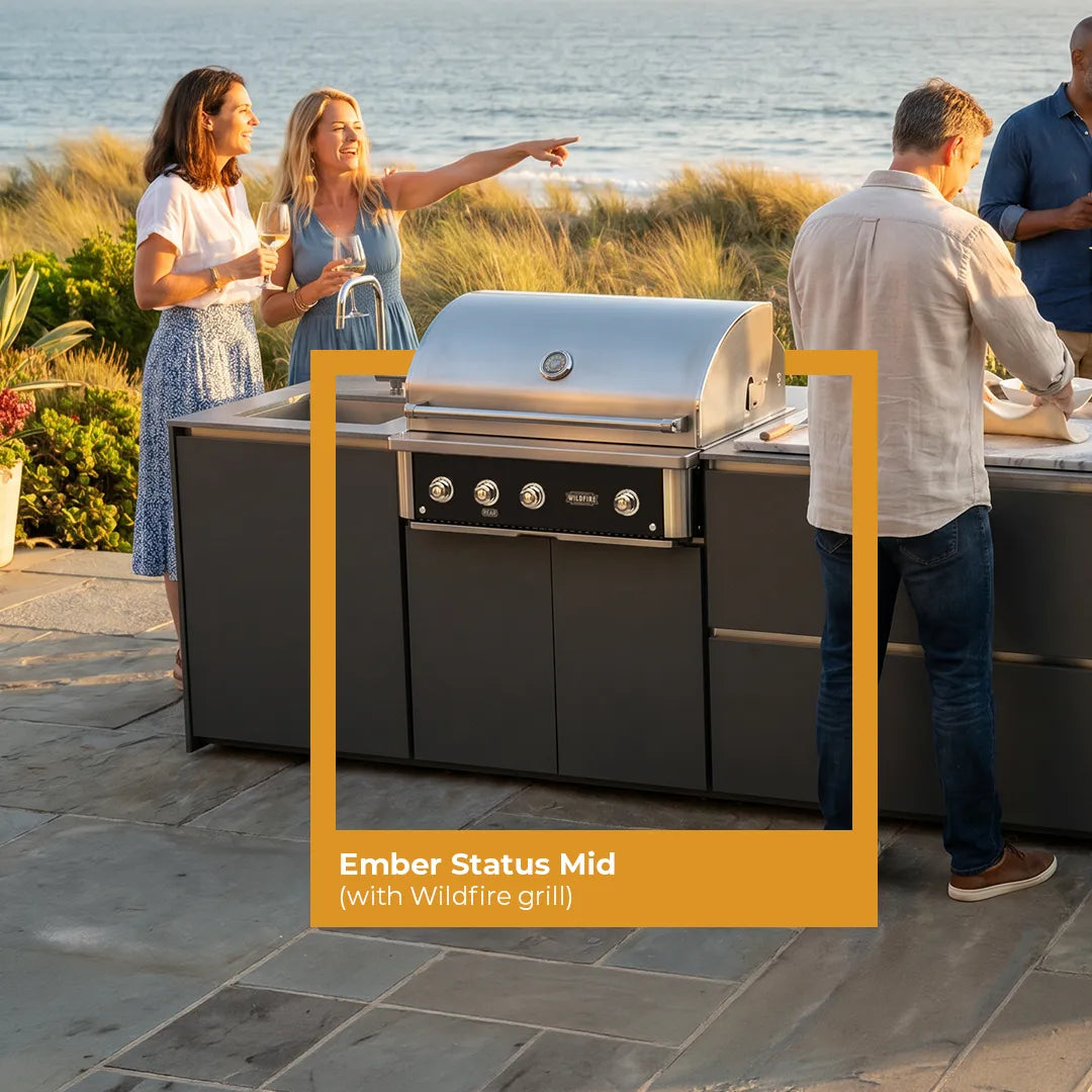 Group of people around a modern Fontana Ember outdoor kitchen with a wildfire grill, set against a scenic ocean backdrop.